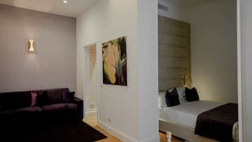 A modern hotel room with a dark-colored sofa, a bed with a headboard, and a painting on the wall.