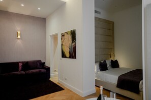 A modern hotel room with a dark-colored sofa, a bed with a headboard, and a painting on the wall. - Màs Boutique Hotel (Rome)