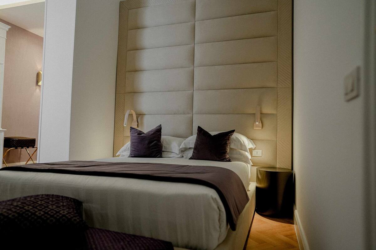 A modern hotel room with a large bed, a headboard with built-in lighting, and a bedside table with a lamp.