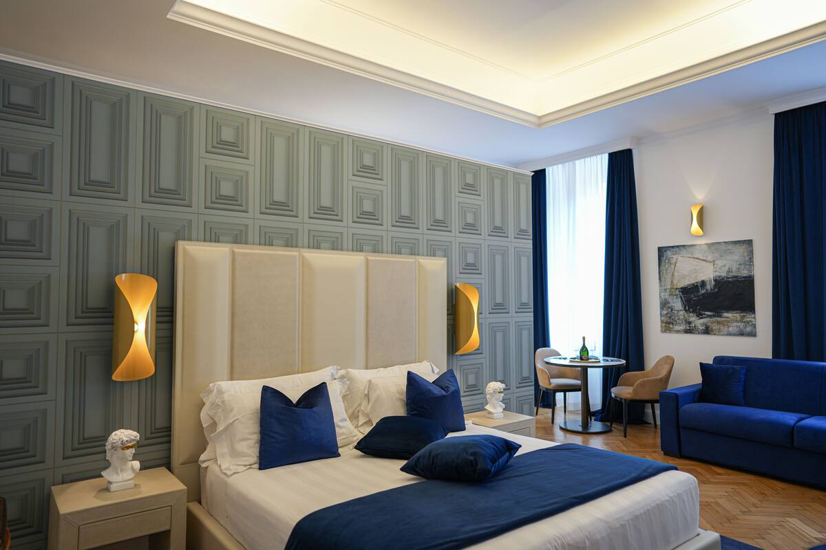 A hotel room with a large bed, a blue sofa, a small table, and a chair.