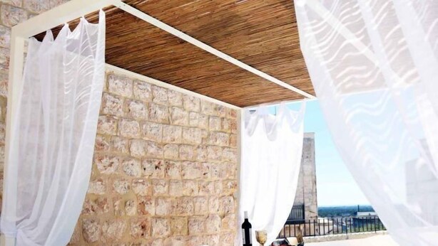 Una piscina infinita con cortinas blancas y un muro de piedra de fondo.