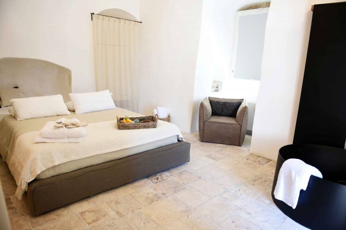 A bedroom with a bed, a chair, a black bathtub, and a window.