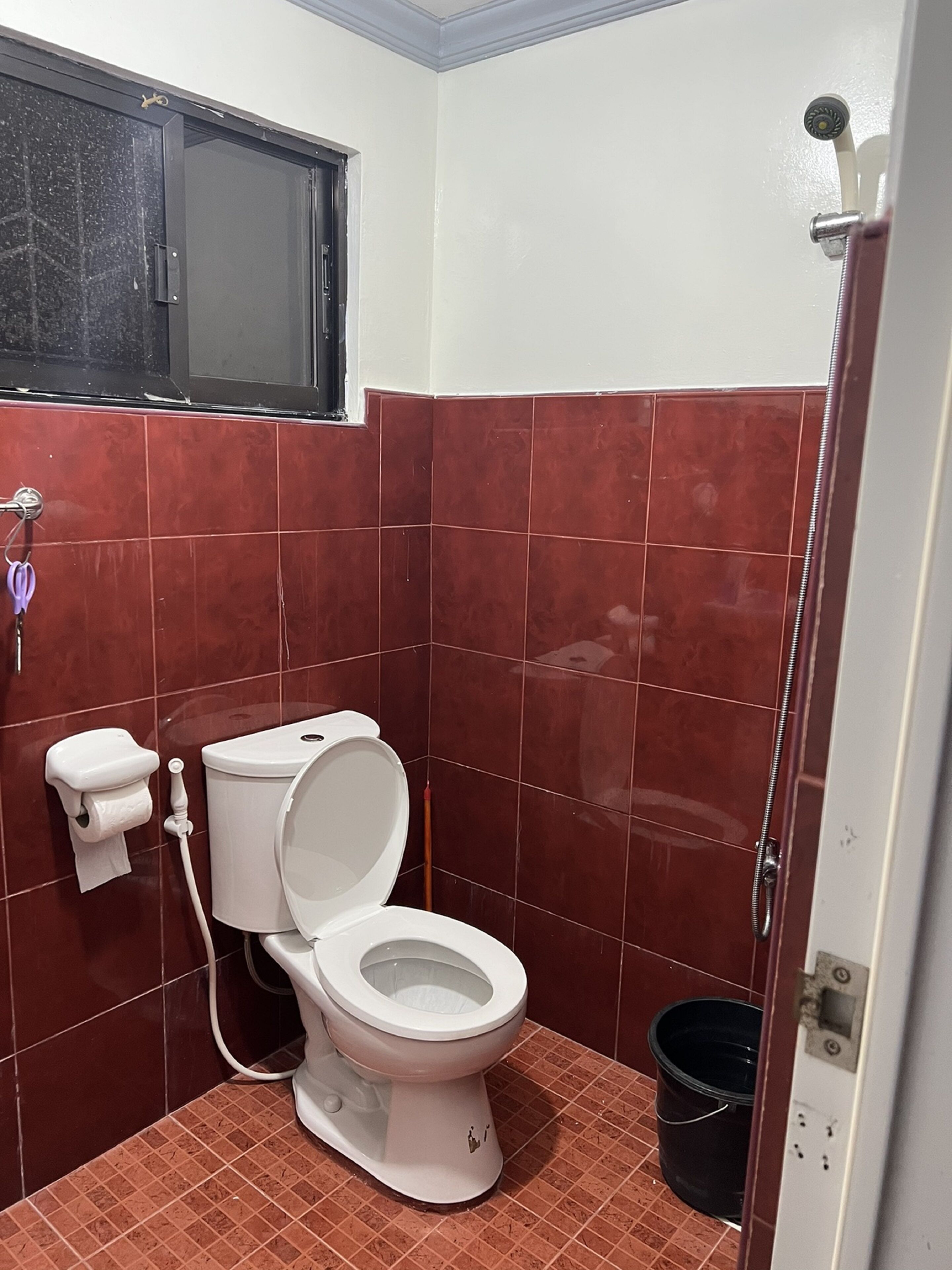 A small bathroom with a toilet, a window, and a shower.