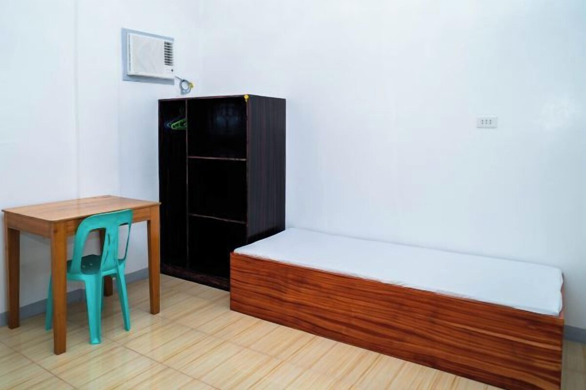 Een kleine kamer met een houten tafel, een turquoise stoel, een zwarte garderobe en een houten bank met een wit kussen.