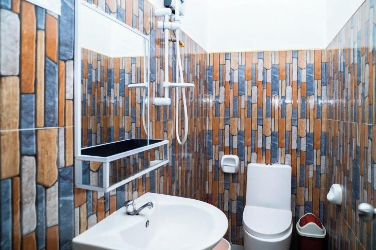 Een badkamer met een wand met stenen patroon, een witte wastafel, toilet en douche.