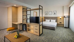 A hotel room with a bed, a TV, a desk with a fruit bowl, a wardrobe, and a bedside table.