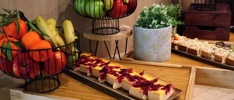Una mesa de buffet con cestas de fruta, una bandeja de pastel de queso y una planta decorativa.