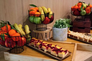 A buffet table with fruit baskets, a tray of cheesecake, and a decorative plant.