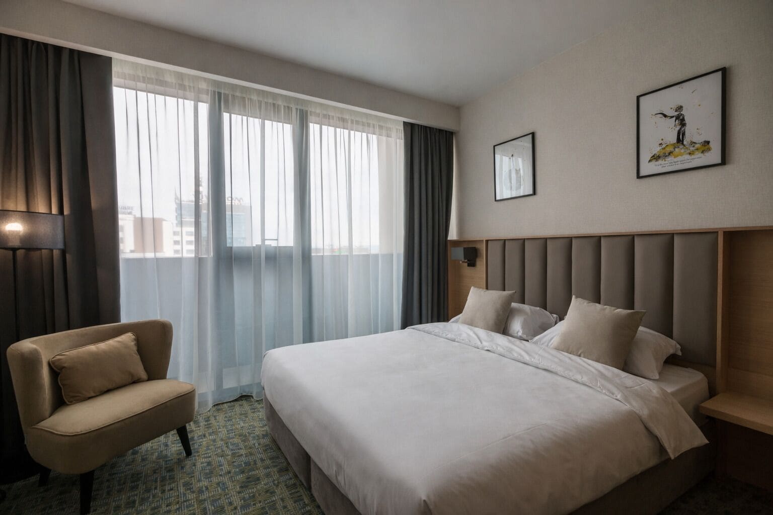 Habitación de hotel con cama, una silla, mesita de noche, lámpara y ventana con cortinas.