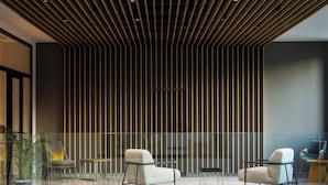 A modern reception area with a slatted ceiling, a glass partition, and seating.