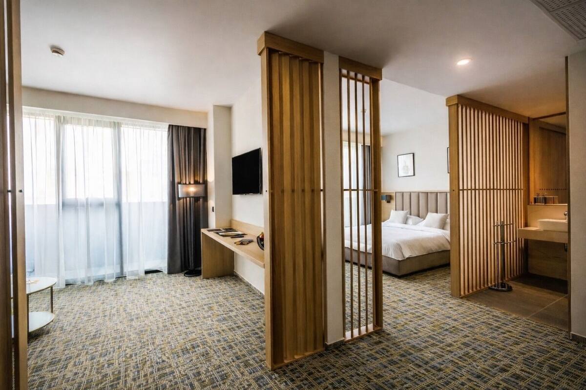 A hotel room with a bed, a desk, a TV, a bathroom, and a view of the outside.