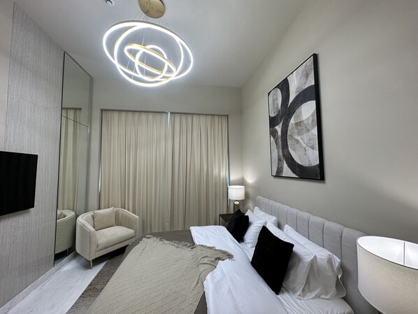 A modern hotel room with a large bed, a sofa, a flat-screen TV, a ceiling light fixture, and a large abstract painting on the wall.