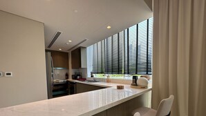 A modern kitchen with a large island, bar stools, and a window with blinds. - Manzil 4BR Penthouse in Dubai Creek w Harbour View (Dubai)