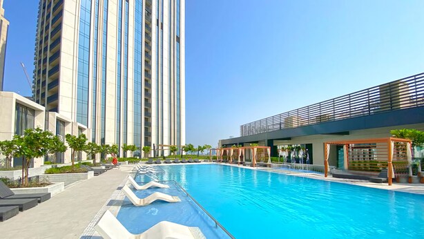 A swimming pool with a modern design, surrounded by high-rise buildings and a covered area with seating. - Manzil 4BR Penthouse in Dubai Creek w Harbour View (Dubai)