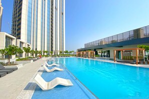 A swimming pool with a modern design, surrounded by high-rise buildings and a covered area with seating.