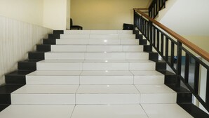 Una escalera con escalones de colores blanco y negro alternados, una barandilla de madera y una pared de color beige al fondo.