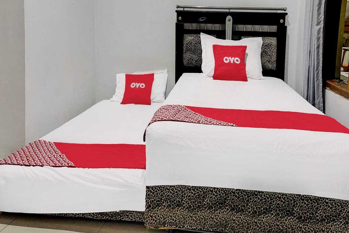 Ein Doppelbett mit zwei roten Kissen, weißer Bettwäsche und einer Decke mit Leopardenmuster.
