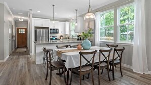 A modern kitchen with white cabinets, stainless steel appliances, and a dining area with a table set for six. - Paradise Point Lakefront Getaway, Beach, Hot Tub (Mabank)