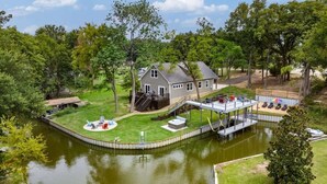 A house with a dock extending into a pond, surrounded by lush greenery. - Paradise Point Lakefront Getaway, Beach, Hot Tub (Mabank)