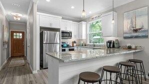 A modern kitchen with white cabinets, stainless steel appliances, a marble island, and bar stools. - Paradise Point Lakefront Getaway, Beach, Hot Tub (Mabank)