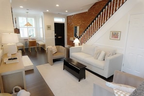 A living room with a white sofa, a coffee table, a fireplace, and a staircase.