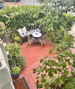A patio with a round table and four chairs, surrounded by potted plants and greenery.