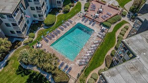 Vue aérienne d’un hôtel moderne doté d’une piscine centrale, entourée de transats et d’une zone aménagée pour se détendre.