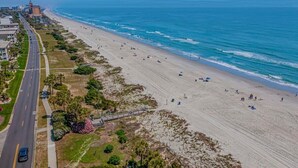 Une vue aérienne d’une plage, avec une route qui la longe, un pont et des bâtiments en arrière-plan.