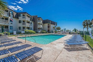 Un hotel con piscina, tumbonas y un cielo azul despejado.