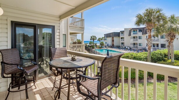 A balcony with wicker chairs and a table, overlooking a pool and other buildings. - Ocean Forest Villas Unit D215 - Ocean view (Myrtle Beach)