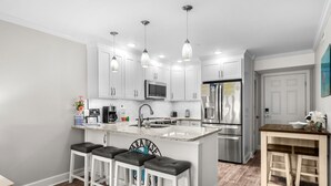 A modern kitchen with white cabinets, stainless steel appliances, and a central island with bar stools. - Ocean Forest Villas Unit D215 - Ocean view (Myrtle Beach)