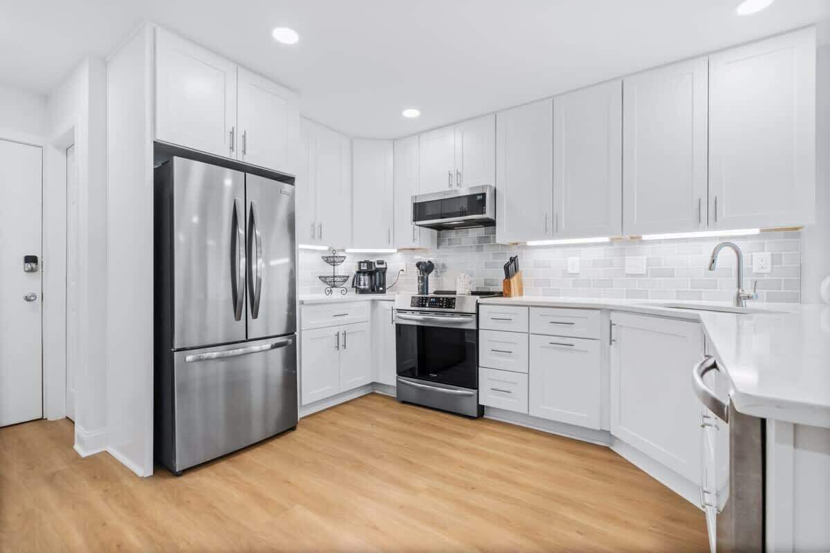A modern kitchen with white cabinets, stainless steel appliances, and a wooden floor.