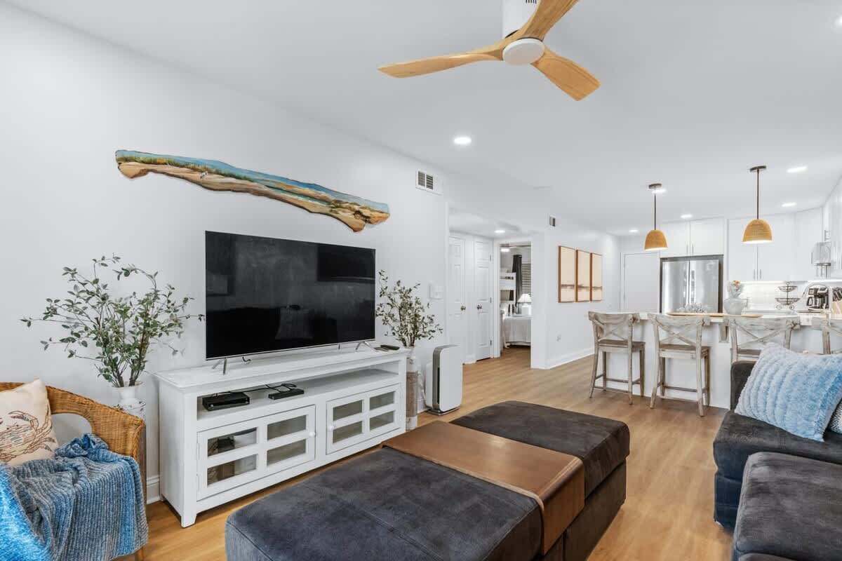 A modern living room with a flat-screen TV, wooden ceiling fan, and a dining area with a bar.