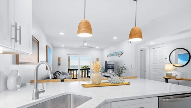 Une cuisine moderne dotée d’un grand îlot central, d’appareils électroménagers en acier inoxydable et de luminaires suspendus.