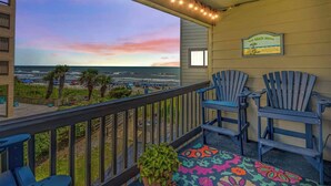 Un balcon avec vue sur la plage, deux fauteuils Adirondack et une pancarte indiquant : « Notre maison de plage ».