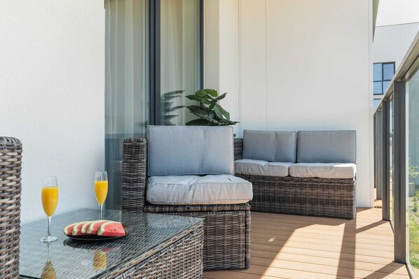 Een balkon met rieten meubels, een glazen tafel en twee glaasjes sinaasappelsap.