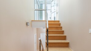 Un escalier avec des marches en bois et une rampe en métal, menant à un palier avec une porte blanche et un petit luminaire fixé au mur.