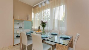 Un espace repas avec une table en verre, des chaises blanches et un buffet doté d’étagères en verre.