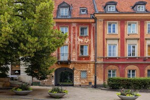 Un bâtiment historique à la façade rouge, doté de nombreuses fenêtres et surmonté d’un grand arbre en premier plan.