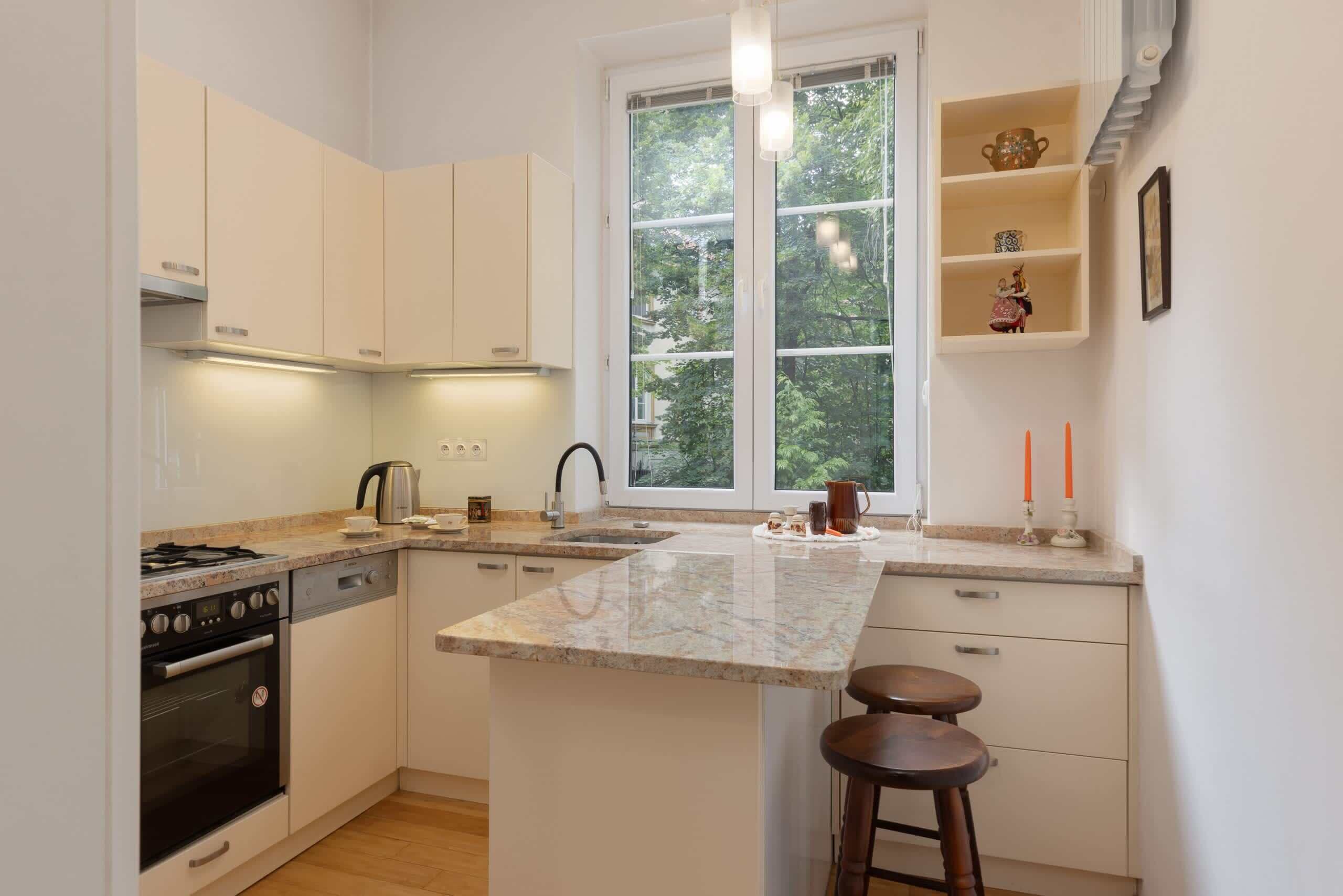 Eine moderne Küche mit weißen Schränken, einer Granit-Arbeitsplatte, einem eingebauten Backofen und einem Fenster mit Blick auf Bäume.