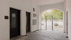 A hallway with a cobblestone floor, a black door, and a metal gate leading to an outdoor area.