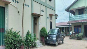 A building with a green facade, a parked truck, and a balcony with potted plants. - Hotel O Aida Lestari (Sebulu)