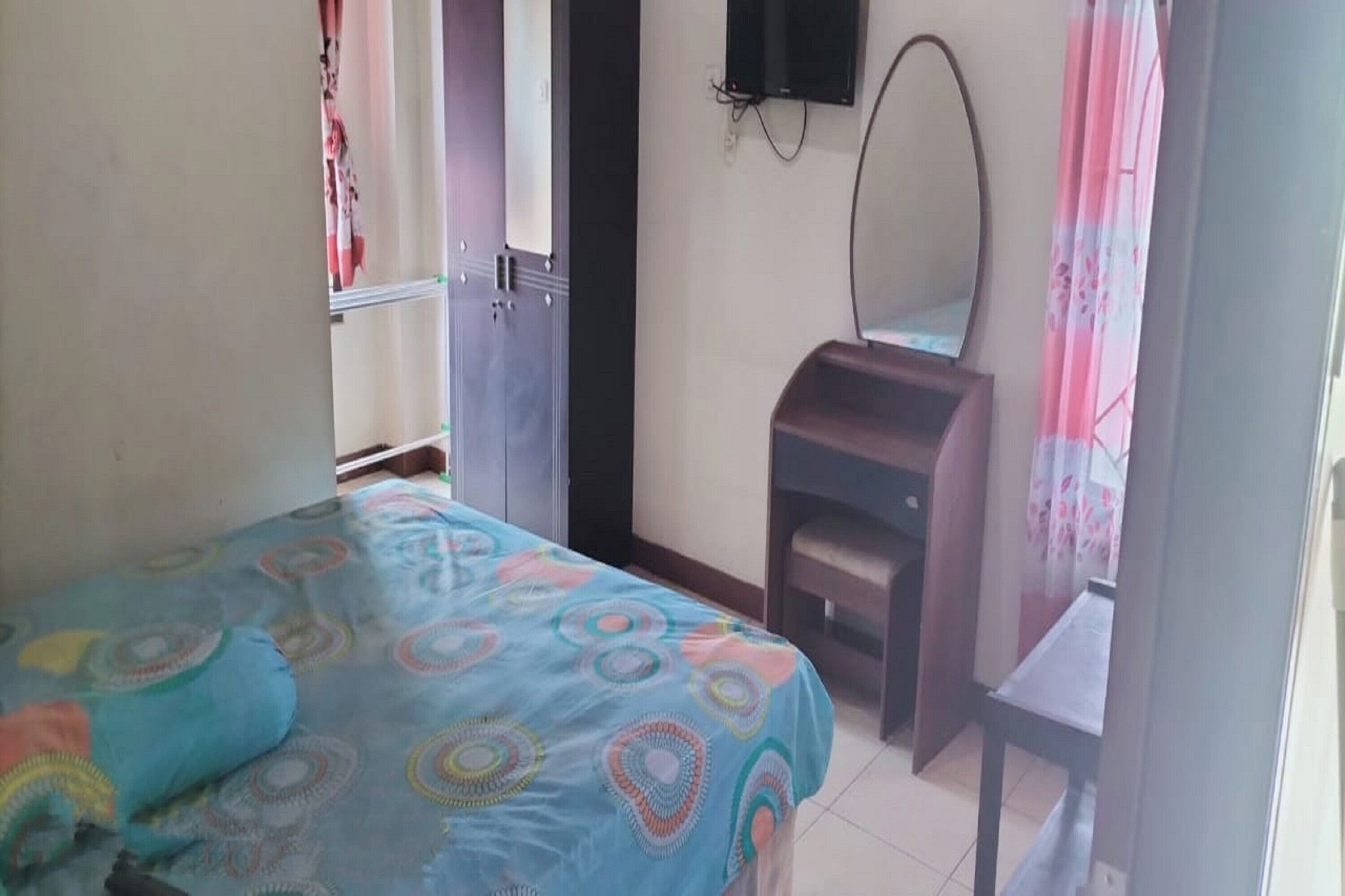 A bedroom with a bed, a dresser, a mirror, and a television on the wall.