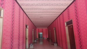 A corridor with pink patterned walls and a tiled floor, leading to a door at the end. - Hotel O Aida Lestari (Sebulu)