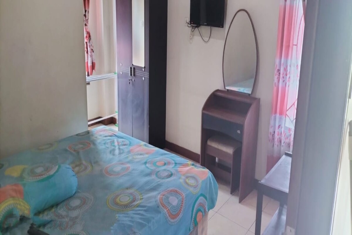 A bedroom with a bed, a dresser, a mirror, and a television on the wall.