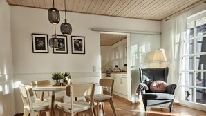 Zona pranzo con tavolo e sedie in legno, un divano e un'ampia finestra con tende.
