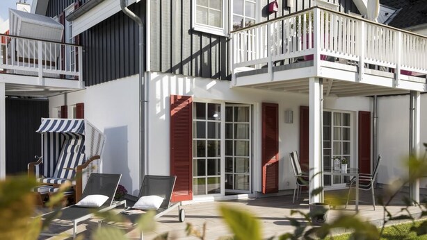 A modern two-story building with a balcony, outdoor seating area, and a covered patio. - 1 - 4 Personen EG, Haustiere Willkommen Terrassenausrichtung Süd und West 2 Schlafzimmer, 1 Badezimmer mit Whirlpool und Dusche (Greetsiel)