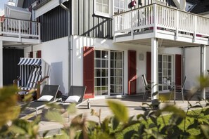A modern two-story building with a balcony, outdoor seating area, and a covered patio. - 1 - 4 Personen EG, Haustiere Willkommen Terrassenausrichtung Süd und West 2 Schlafzimmer, 1 Badezimmer mit Whirlpool und Dusche (Greetsiel)