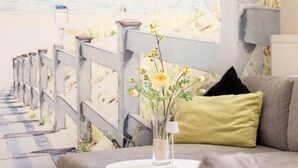 A cozy seating area with a round table, a vase with yellow flowers, and a grey sofa with a green cushion. - 1 - 4 Personen EG, Haustiere Willkommen Terrassenausrichtung Süd und West 2 Schlafzimmer, 1 Badezimmer mit Whirlpool und Dusche (Greetsiel)