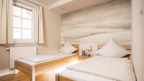 A bedroom with two beds, a window with curtains, a radiator, and a wall-mounted lamp. - 1 - 4 Personen EG, Haustiere Willkommen Terrassenausrichtung Süd und West 2 Schlafzimmer, 1 Badezimmer mit Whirlpool und Dusche (Greetsiel)